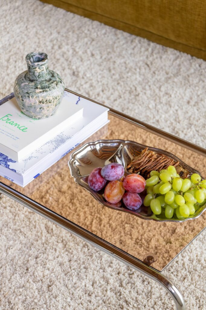 Glazen salontafel met boeken over Frankrijk, een keramische vaas en een vintage zilveren schaal met fruit