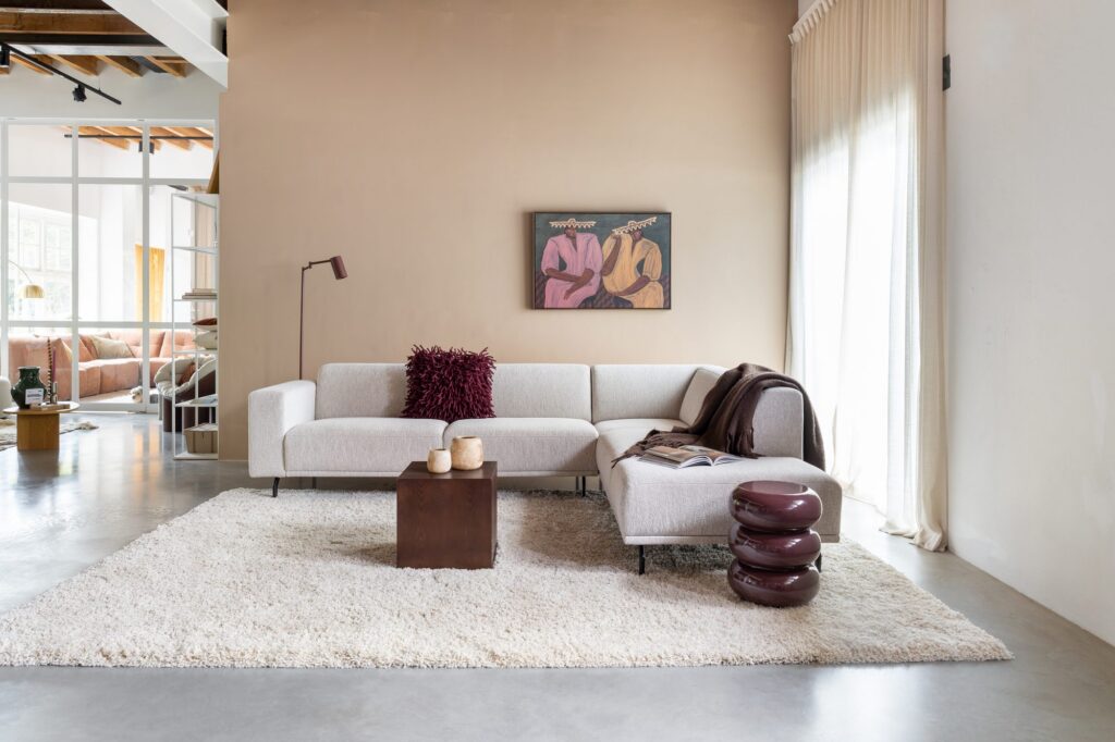 Overzicht van de moderne studio met hoekbank Nivar, schilderij, bordeauxrode bijzettafel en vloerkleed