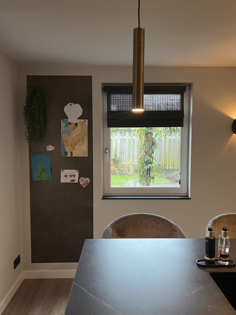 Keukeneiland met zicht op de tuin en een donkere magneetwand met kindertekeningen